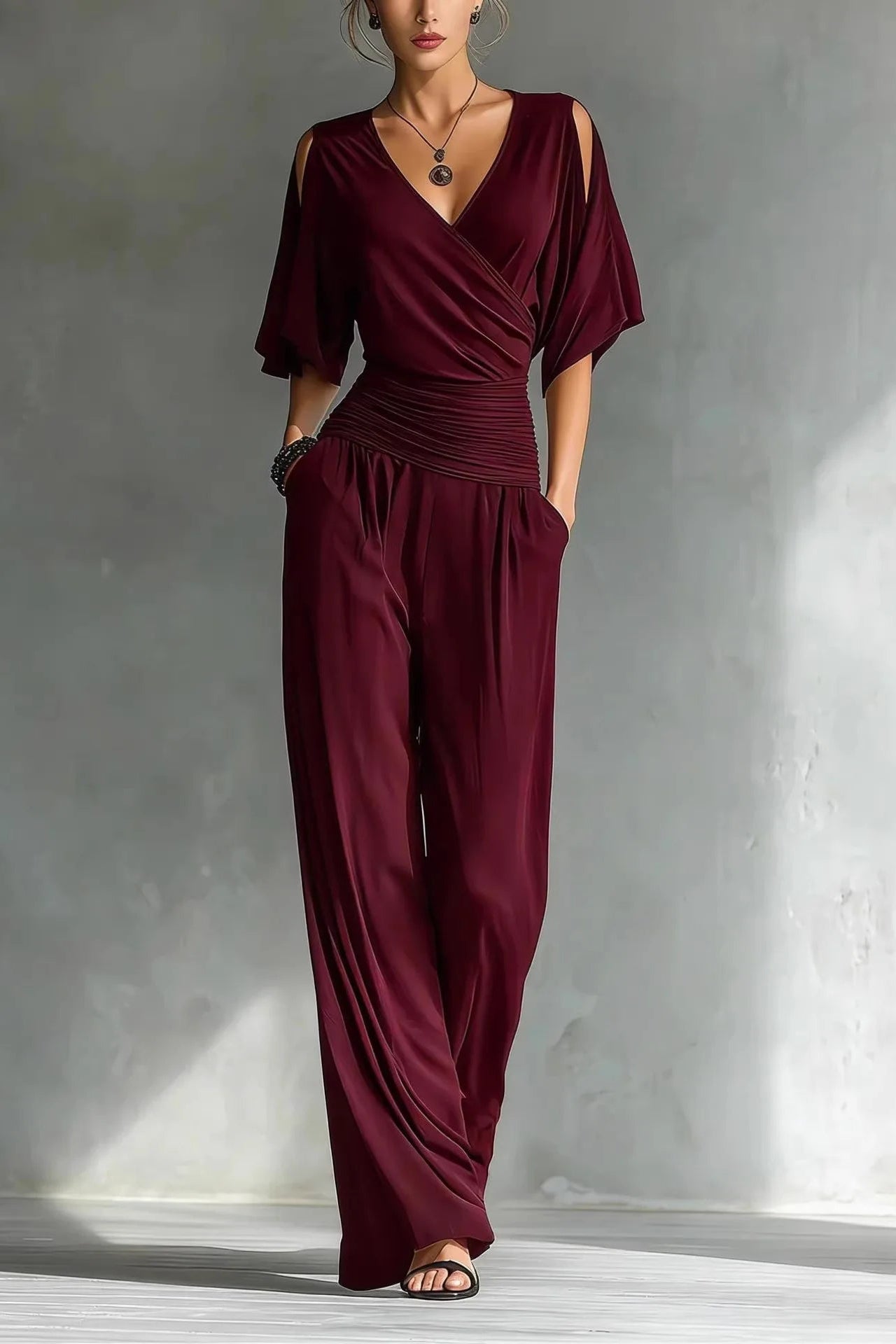 Maroon jumpsuit worn by a model against a gray concrete wall.