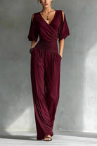 Maroon jumpsuit worn by a model against a gray concrete wall.