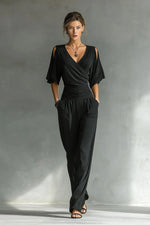 Woman wearing a black jumpsuit against a gray background